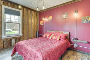 A bedroom with a large bed, a window with a view, a radiator, and artwork on the walls.