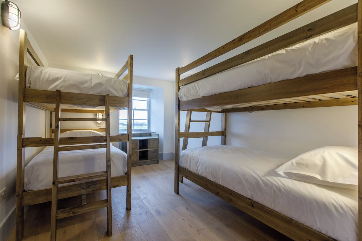 Een kamer met twee stapelbedden, houten vloeren, een raam en een klein bureau met lades.