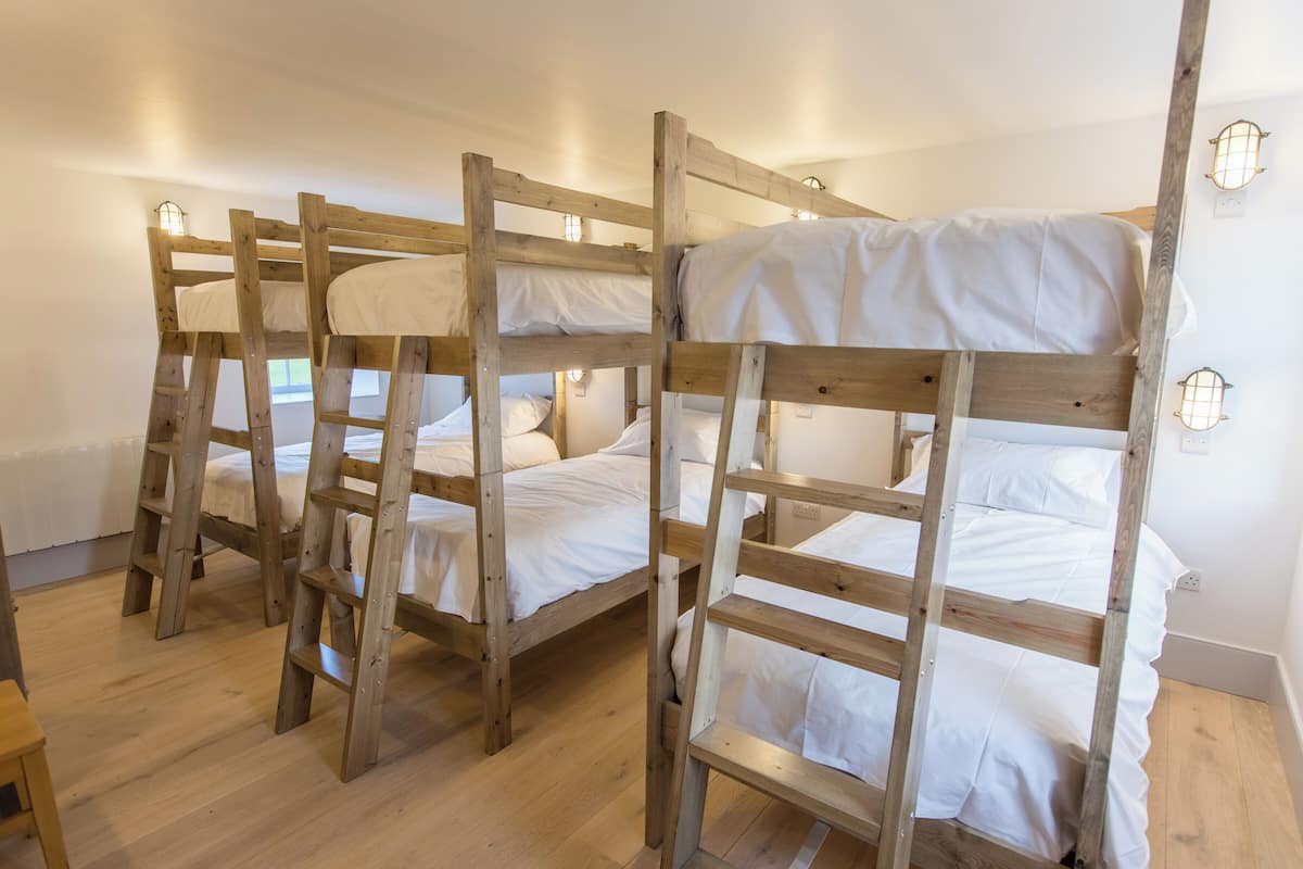 Een kamer met drie houten stapelbedden, elk voorzien van witte beddengoed.