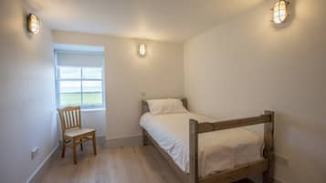 Une petite chambre avec un lit simple, un cadre de lit en bois, une chaise et deux lampes fixées au mur.