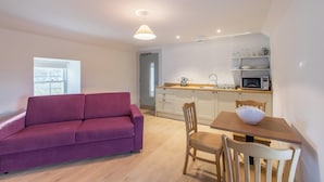 A compact living space with a sofa, dining table, chairs, a kitchen area with a microwave, and a window. - Portsoy Sail Loft (Portsoy)
