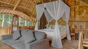 A room with a bed under a canopy, a sofa, and a wooden floor.