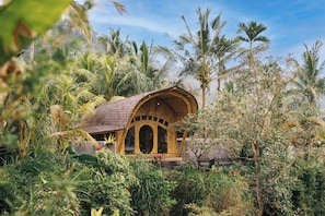 A wooden structure with arched windows surrounded by lush greenery and palm trees. - Aura Cendana Hill Sidemen by AGATA (Selat)