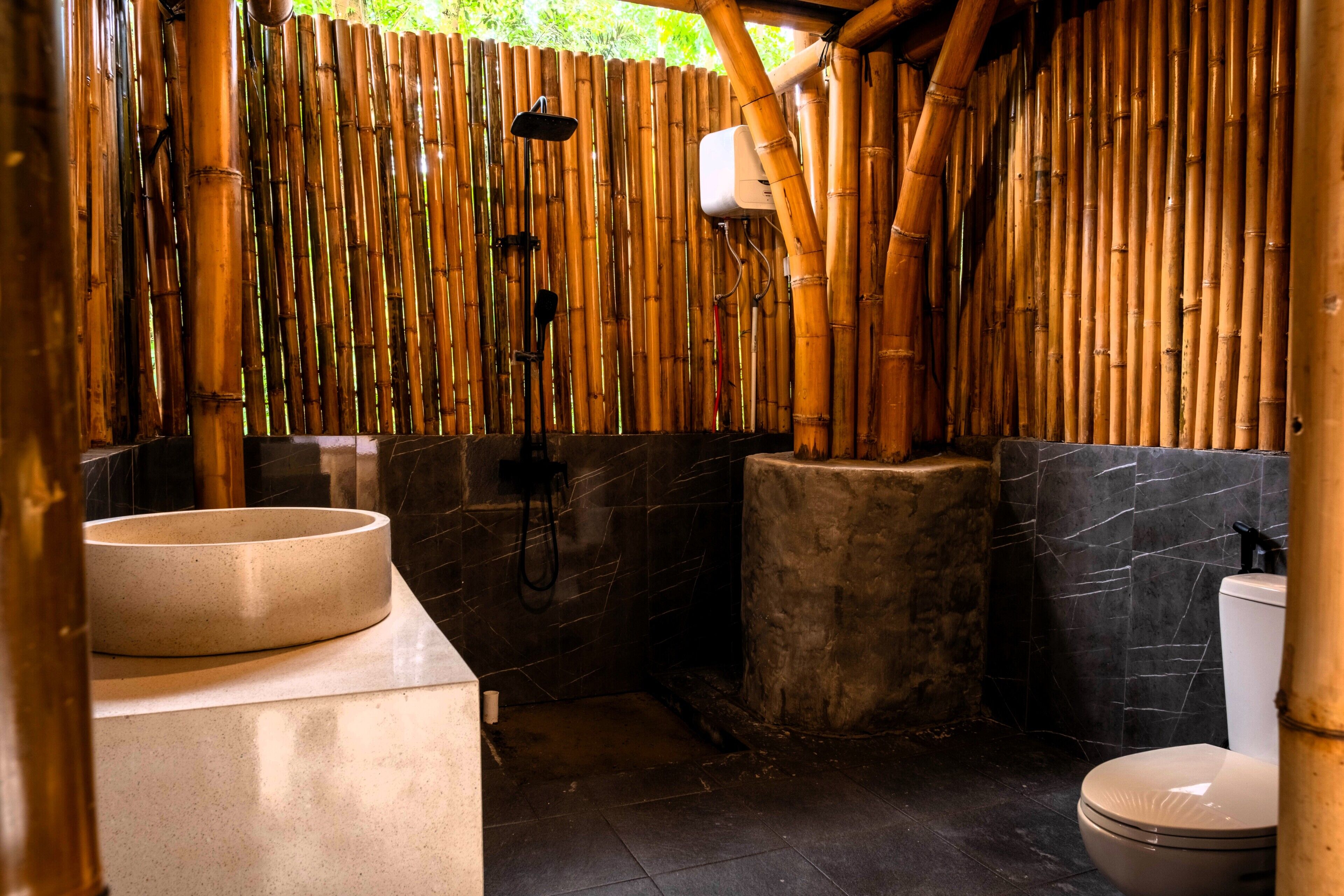 A bathroom with a bamboo wall, a round sink, a toilet, and a shower area.