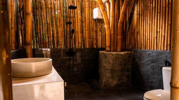A bathroom with a bamboo wall, a round sink, a toilet, and a shower area.