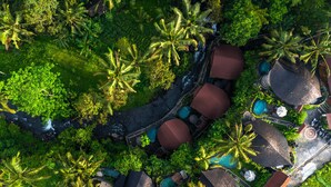 An aerial view of a resort with multiple bungalow-style accommodations, a central pool area, and lush tropical vegetation.