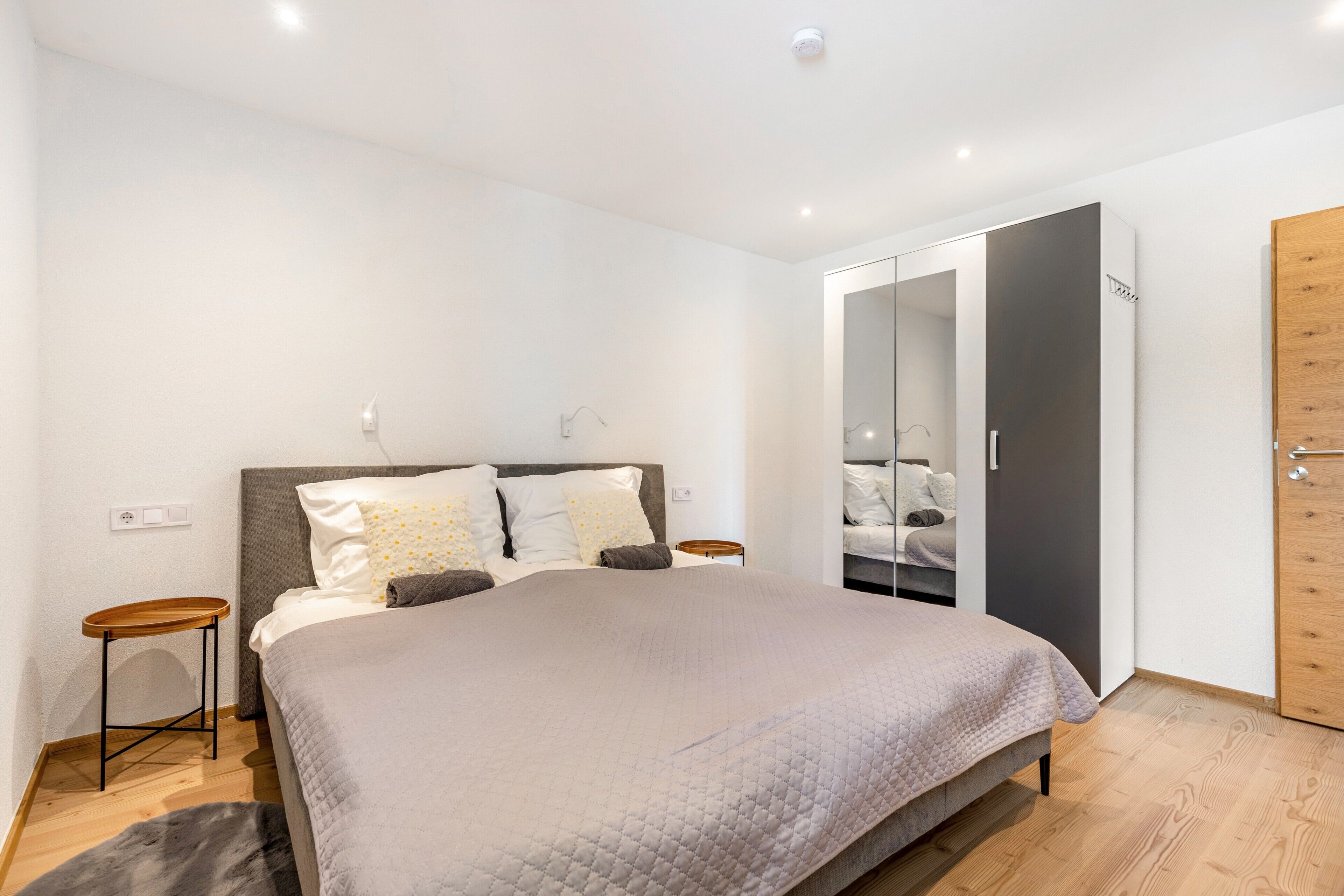 A modern bedroom with a bed, bedside tables, a wardrobe, and a mirror.