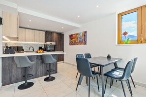 Uma cozinha moderna com bancada de mármore, sala de jantar com mesa e cadeiras, e uma janela grande com vista.