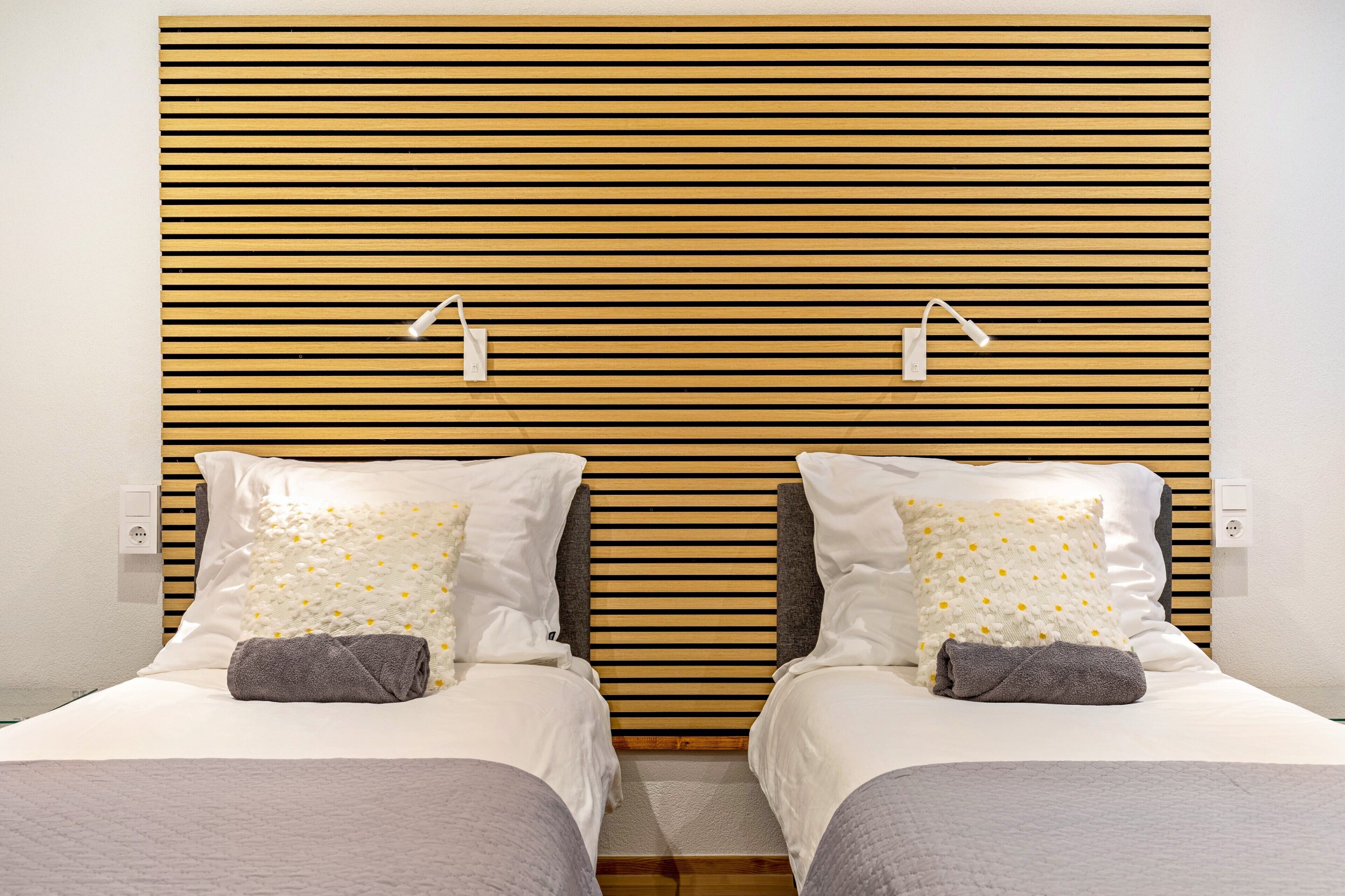 A double bed with a wooden slat headboard, two bedside lamps, and a gray towel on each bed.