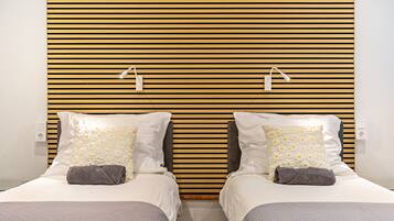 A double bed with a wooden slat headboard, two bedside lamps, and a gray towel on each bed.