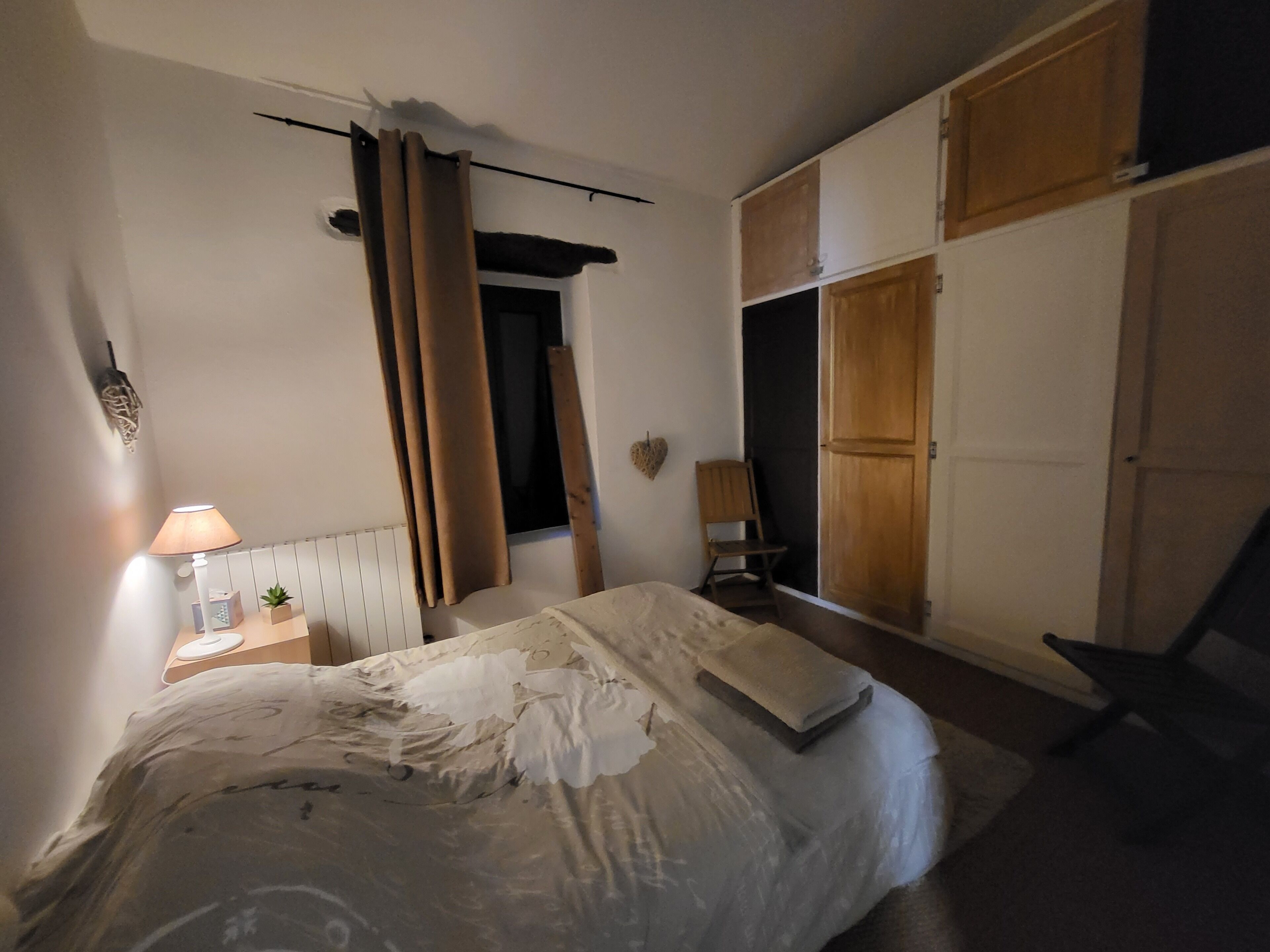 A bedroom with a bed, a nightstand, a lamp, a chair, and a wardrobe.