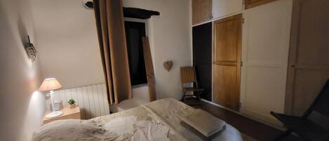 A bedroom with a bed, a nightstand, a lamp, a chair, and a wardrobe.
