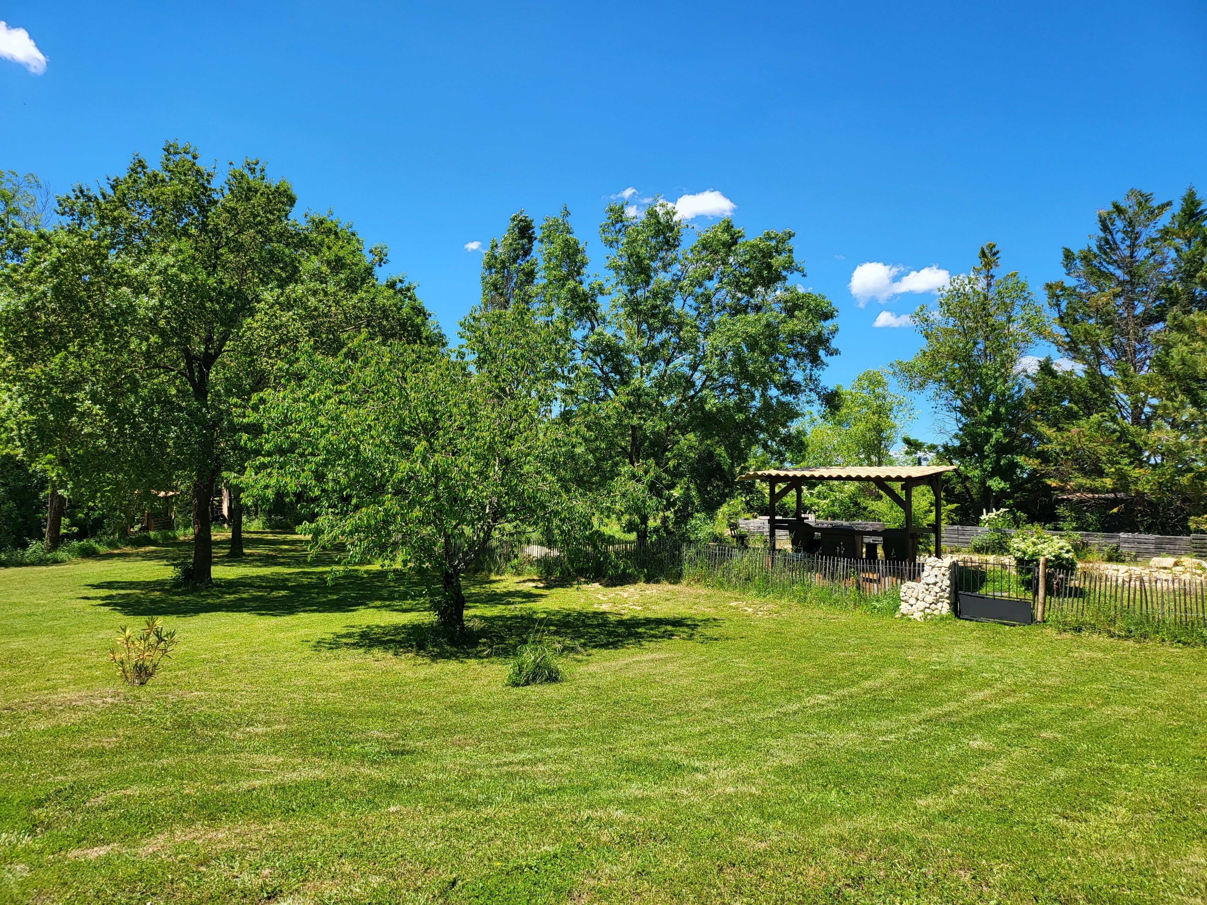 Un parc avec un kiosque, des arbres et un mur de pierre.