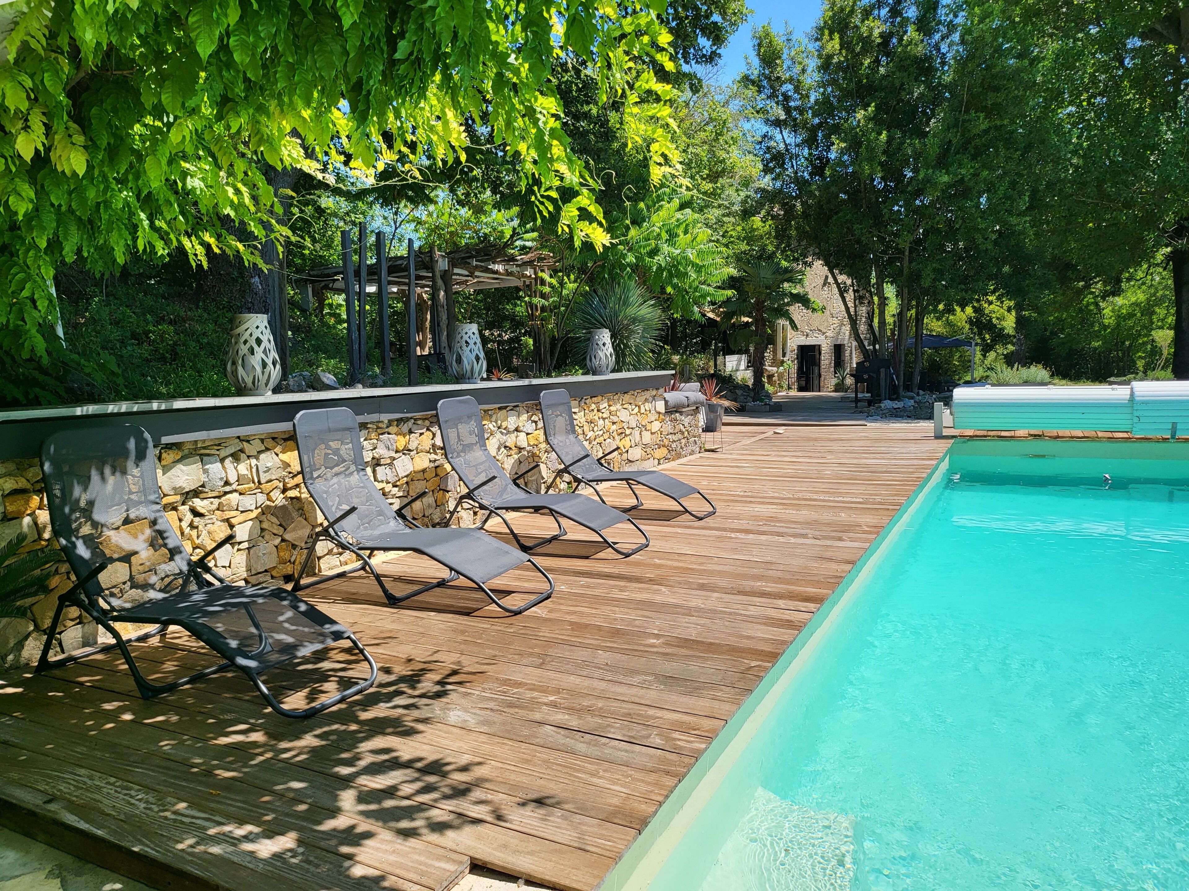 A wooden deck with lounge chairs, a stone wall, and a swimming pool.