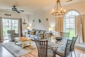 Ein geräumiges Wohnzimmer mit einem Esstisch mit Glasplatte, Holzsesseln, einer Couch und einem Deckenventilator.