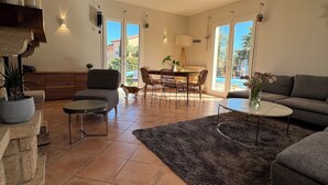 A spacious living room with a fireplace, a dining area, and a large window. - VILLA VUE MER LA FARDELOIE (La Ciotat)