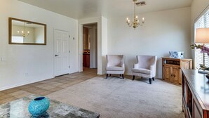 Un salon spacieux agrémenté d’un grand miroir, de deux fauteuils, d’une commode en bois et d’un lustre.