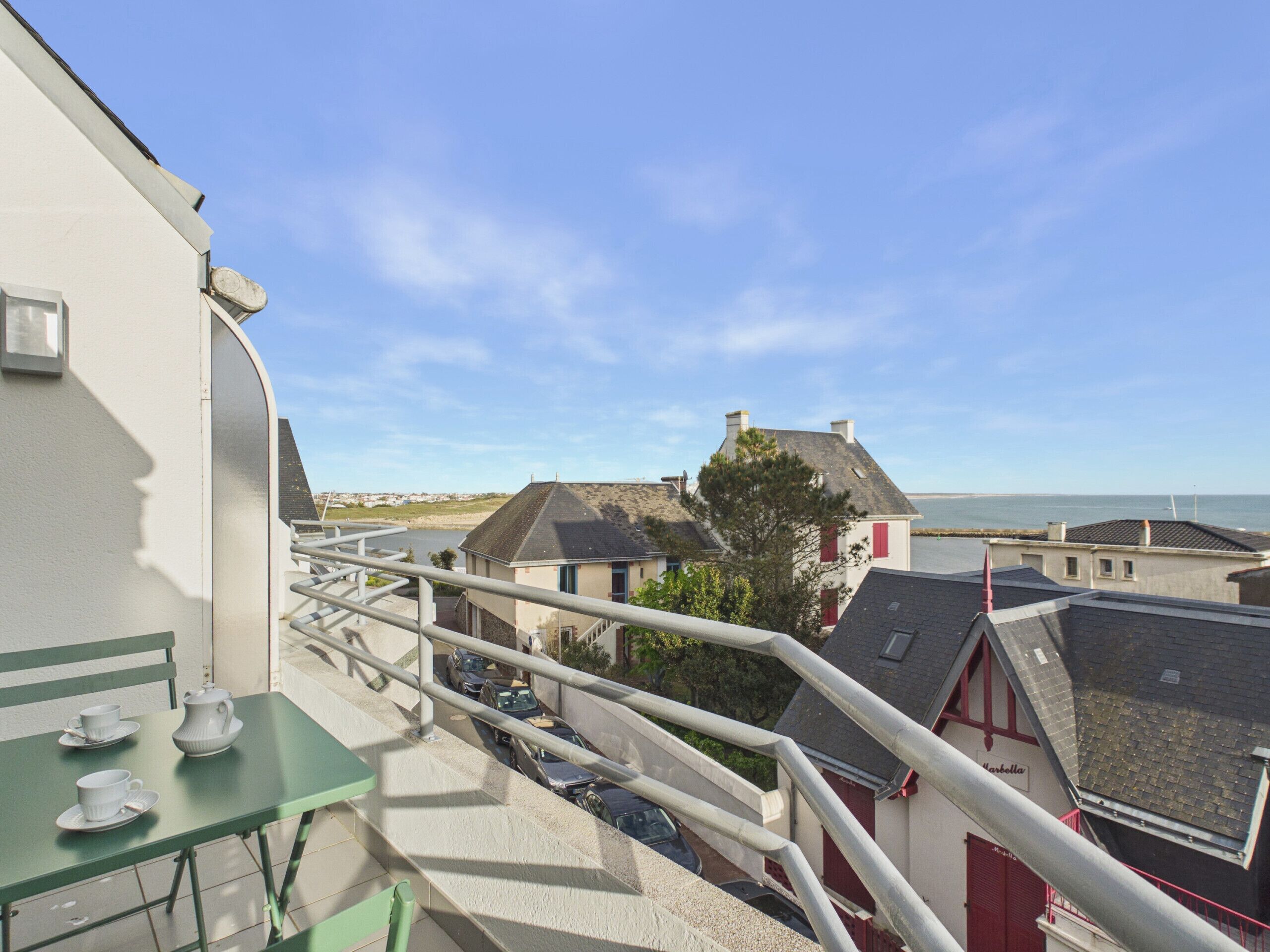 A balcony with a table and chairs, a railing, and a view of houses and a body of water.