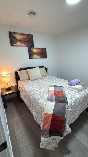 A bedroom with a bed, nightstand, lamp, and two wall-mounted paintings.
