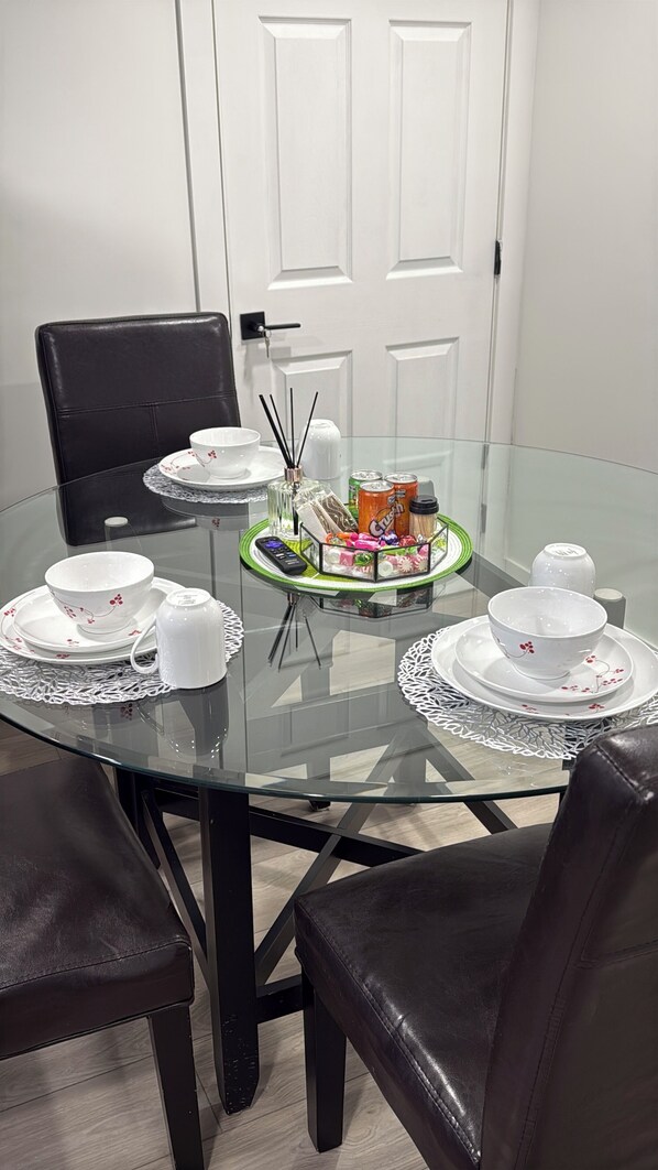 A dining table with glass top, surrounded by chairs, white plates, and a centerpiece with snacks.