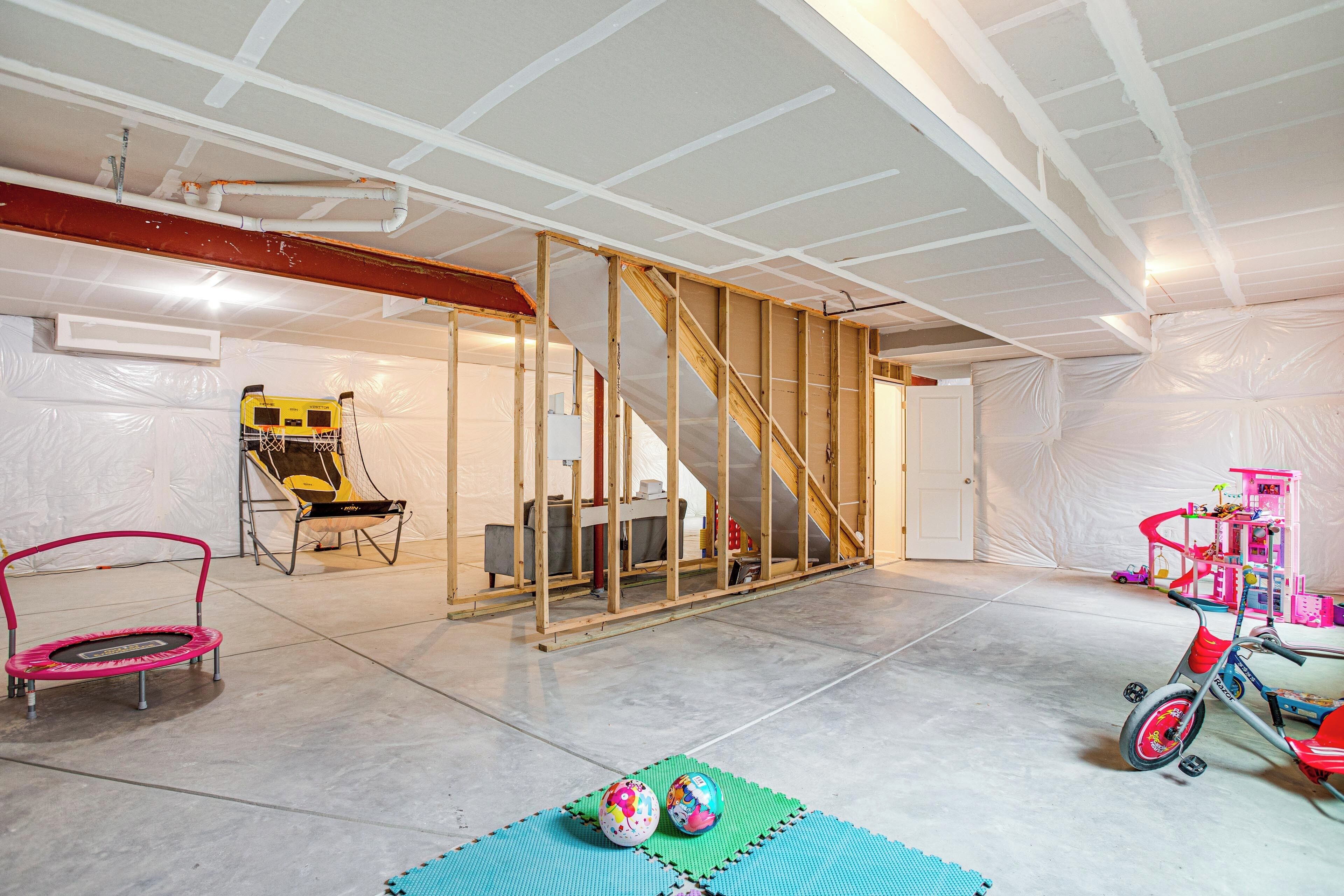 A spacious room with a high ceiling, a wooden staircase, and a play area with a trampoline and a toy train.