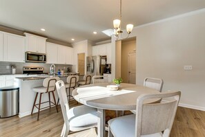 Une cuisine moderne avec des meubles blancs, des appareils en acier inoxydable et un coin repas comprenant une table ronde et des chaises.