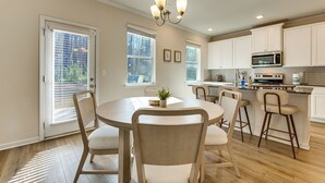 Une cuisine moderne avec des meubles blancs, un îlot central doté de tabourets, un lustre et un coin repas avec des chaises.