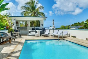 Ein Poolbereich mit Liegestühlen, einer Bar und Blick aufs Meer.