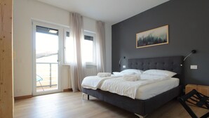 Un dormitorio con cama, un cuadro, una silla y un balcón.