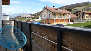 Un balcón con una silla azul, vista a un barrio residencial con casas y una cadena montañosa al fondo.
