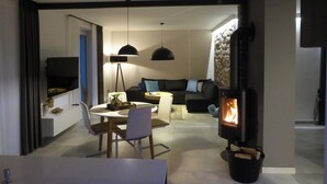 Ein modernes Wohnzimmer mit Kamin, einem Essbereich mit rundem Tisch und Stühlen sowie einer Couch mit Kissen.