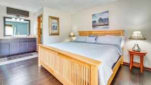 Quarto com cama de madeira, mesa de cabeceira, luminária, cômoda e um quadro na parede.