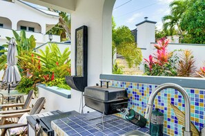 Eine Terrasse mit Grill, Sitzgelegenheiten im Freien und einer gefliesten Rückwand.