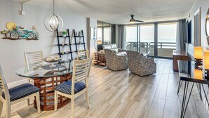 Un salon moderne avec une table à manger en verre, des sièges confortables, un ventilateur de plafond et une grande fenêtre offrant une vue dégagée.