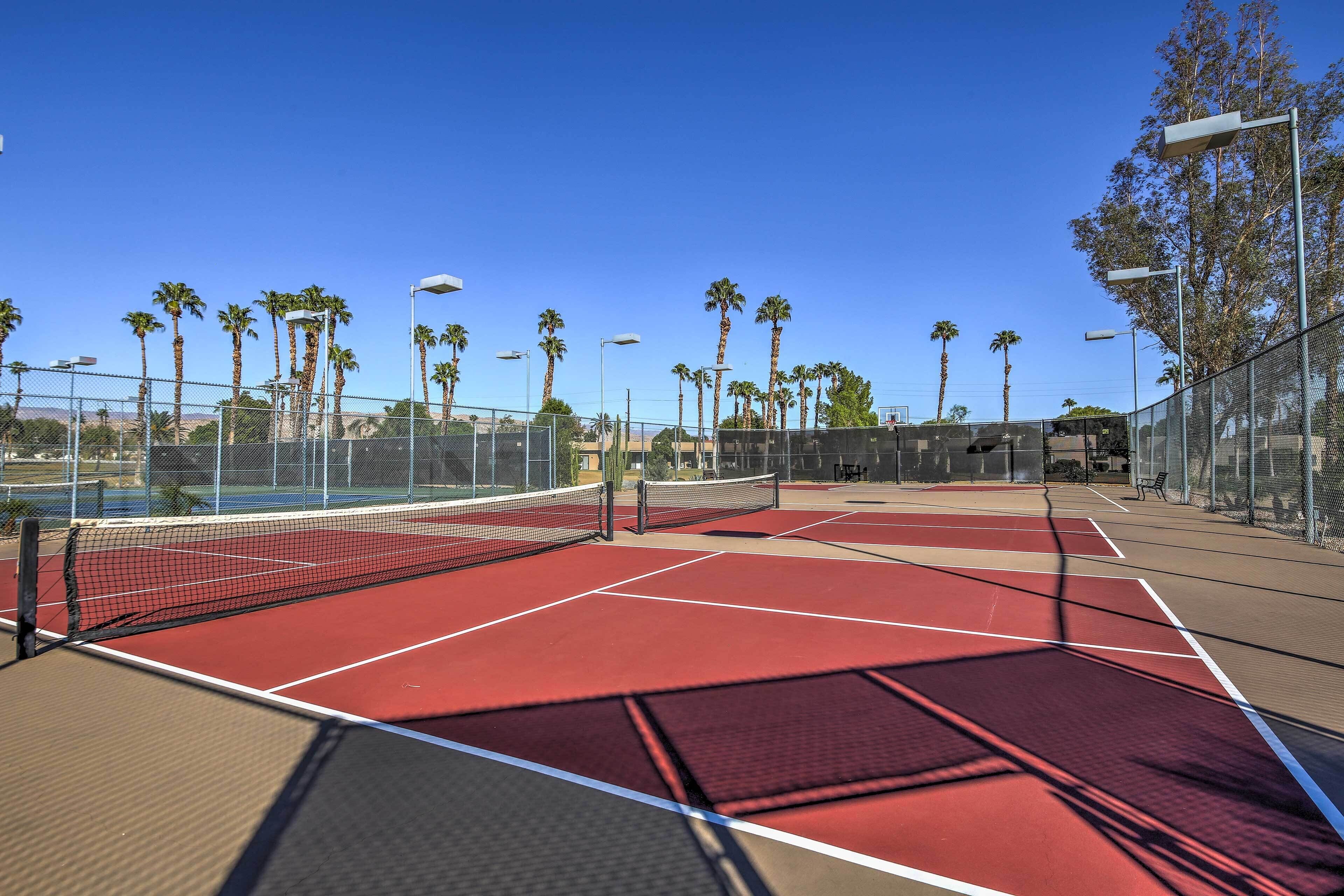 Ein Tennisplatz mit Netz, umzäunt und von Palmen gesäumt.