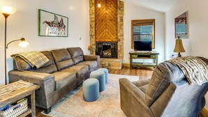 A living room with a fireplace, leather sofas, ottomans, a coffee table, and a television. - Steps to the New Angel Express Lift! Fun Condo (Angel Fire)