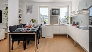 Eine moderne Küche mit weißen Schränken, ein Essbereich mit Tisch für vier Personen und Blick auf die Stadt durch große Fenster.