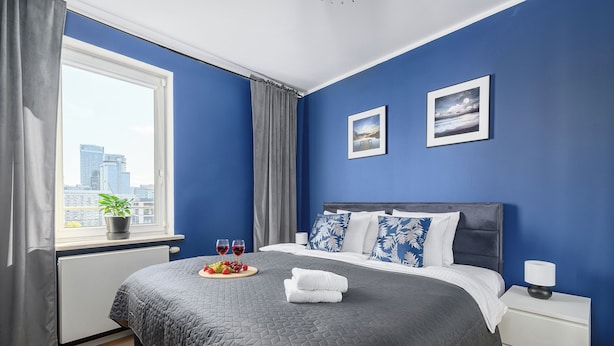 Ein Schlafzimmer mit einem großen Bett, einem Nachttisch, einem Fenster mit Vorhängen und zwei gerahmten Bildern an der Wand.