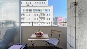 Ein Balkon mit Tisch, Obstschale, Stuhl und Blick auf ein Gebäude.