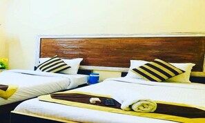A hotel room with two beds, each with striped pillows and a wooden headboard. - Hotel Aanvi Palace (Varanasi)