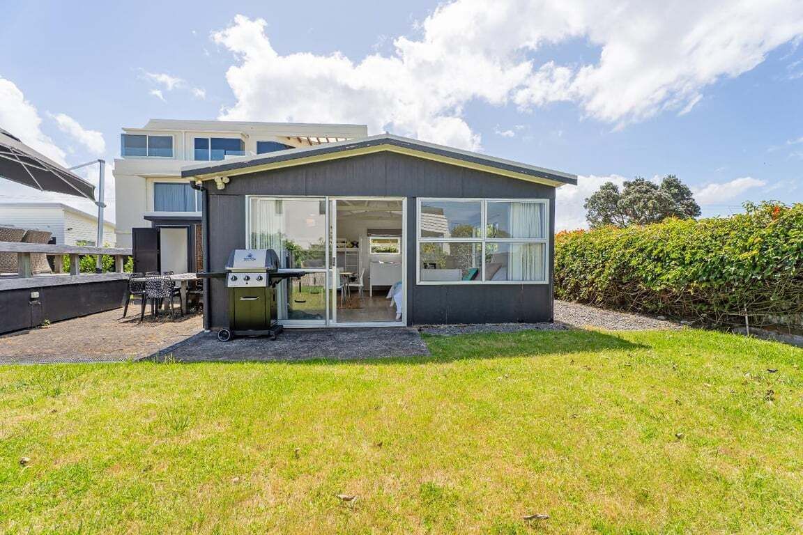 Una casa moderna con un patio, una parrilla y un ventanal que da a un espacio interior.