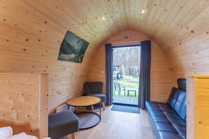 A cozy cabin interior with a wooden ceiling, a round table, a sofa, and a chair. - Zeeland Glamping Lodge for 2 (Burgh-Haamstede)