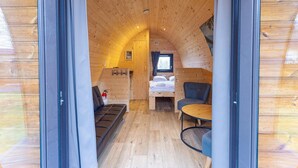 Un interior acogedor de madera con una cama, una silla, una mesita y un ventanal.