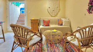 Une pièce comprenant un canapé, deux fauteuils en osier, une décoration murale en macramé et un tapis coloré tissé.