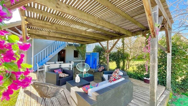 Un espace extérieur aménagé, abrité et doté de meubles en osier, offrant une vue sur une maison.