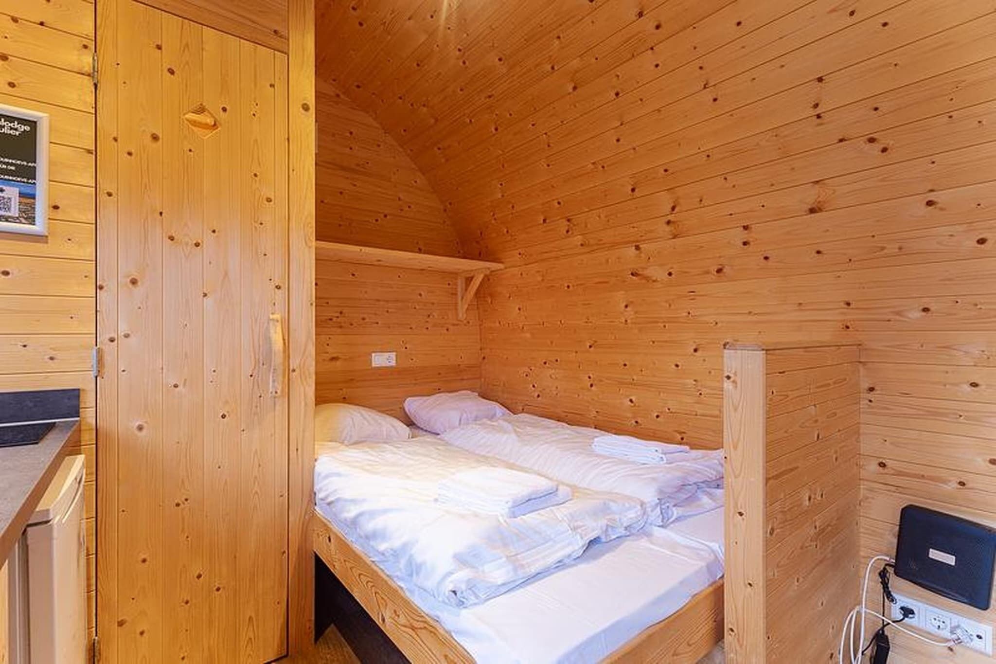 A wooden cabin room with a bunk bed, a small desk, and a power outlet.