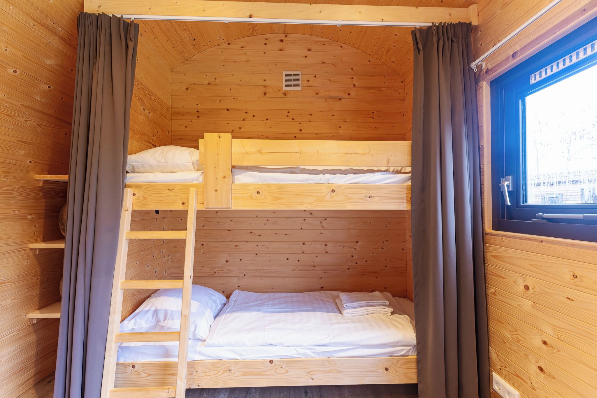 A wooden bunk bed room with a window, curtains, and a ladder.