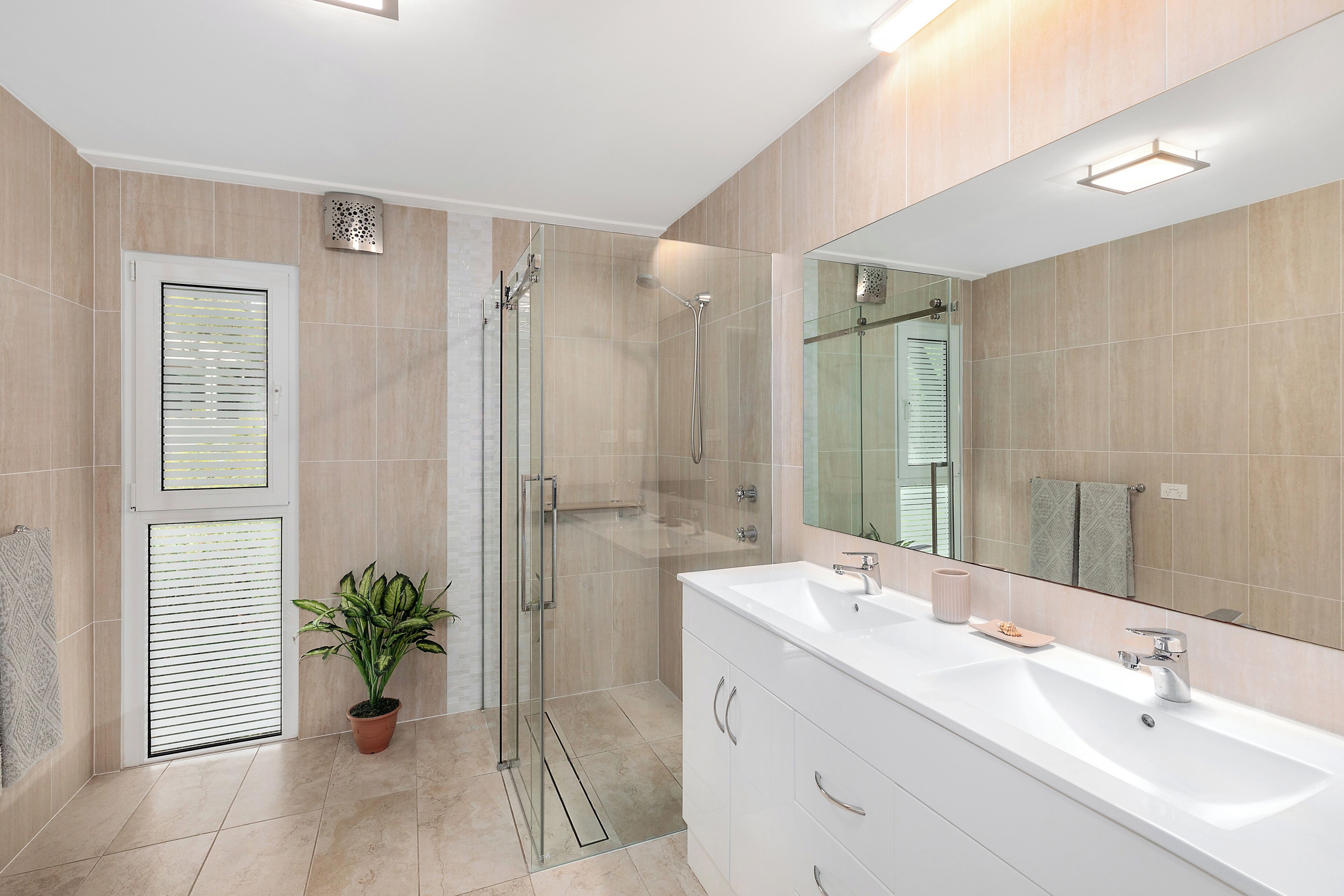 A modern bathroom with a glass shower enclosure, a white vanity with a large mirror, and a potted plant.