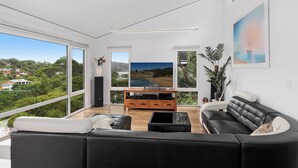 Una sala de estar moderna con un ventanal grande, un mueble de entretenimiento de madera y un sofá de cuero negro.