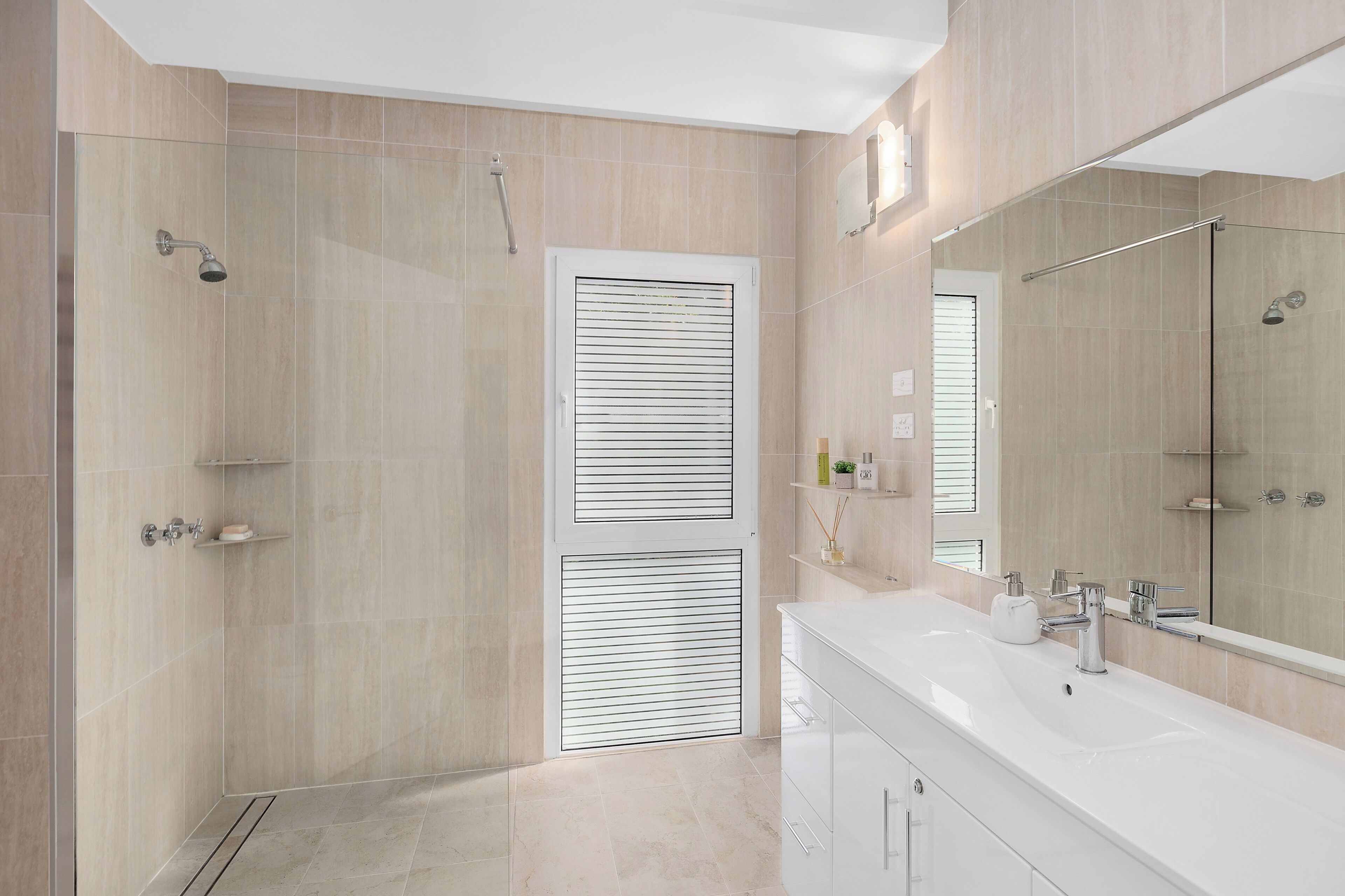 A modern bathroom with a walk-in shower, a large mirror, and a white vanity.
